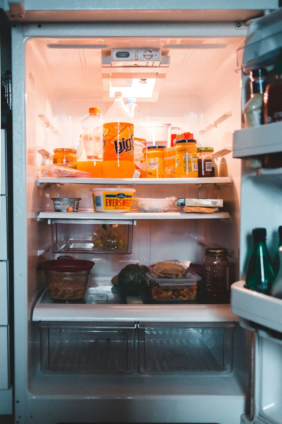 An open refrigerator with jars, drinks, and food containers on its shelves